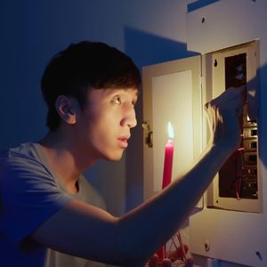 Man holding candle in the dark at electrical panel
